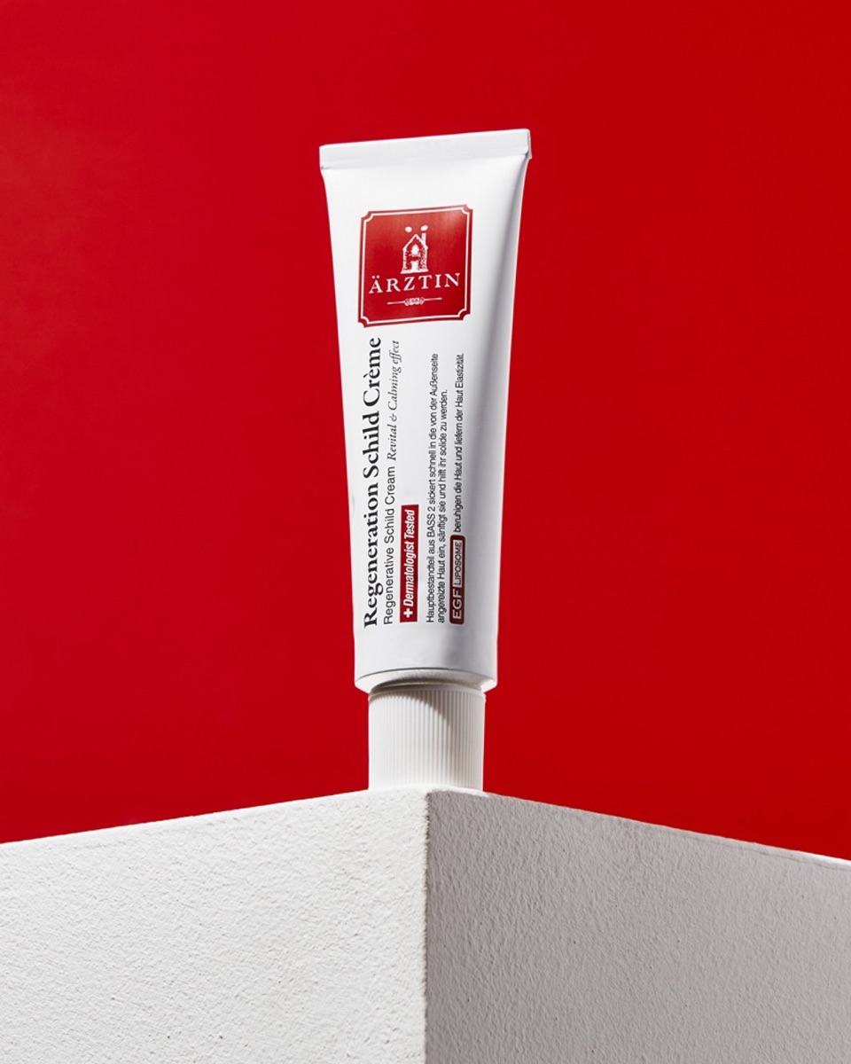 Ärztin Regenerative Schild Cream tube on a white block against a red backdrop
