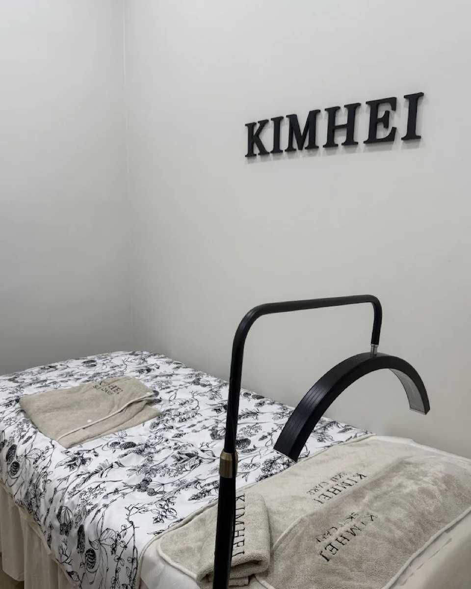 KIMHEI treatment room with a floral-linen bed, branded towels and a device arm